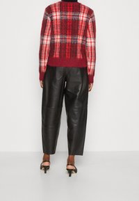 Pull en tricot à carreaux rouge et gris, de coupe courte, associé à un pantalon en cuir noir taille haute. Des talons noirs complètent le look.