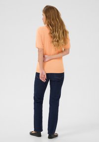 Haut pêche à manches courtes, texture douce, associé à un jean bleu foncé, coupe droite, design simple et ballerines noires. Vue de dos.