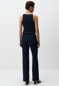 Completo a due pezzi in maglina a coste blu navy, composto da un top senza maniche e pantaloni svasati. Il tessuto ha una finitura testurizzata ed è aderente.