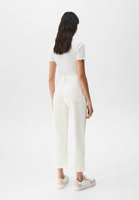 Top bianco a maniche corte con bordo scallop abbinato a jeans bianchi a vita alta e cropped con orli sfrangiati, indossati con sneakers beige e bianche.