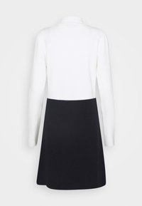 Abito a maniche lunghe con parte superiore bianca e gonna nera, realizzato in tessuto morbido. Presenta un colletto e una texture liscia all'orlo.