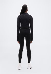 Μαύρο αθλητικό τοπ μακρυμάνικο και εφαρμοστά κολάν με ζώνη μέσης «NIKE PRO». Ομαλή υφή, απλός σχεδιασμός, συνδυασμένο με λευκά αθλητικά παπούτσια.