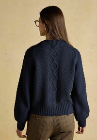 Jūras spēku zilas adītas džemperis ar teksturētām rakstām, puffētiem piedurknēm un ribotajiem aprocēm. Iemācīts centrālais kabelis dizains pa muguru.