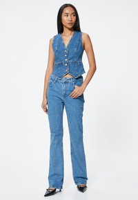 Chaleco de denim en azul claro, con un escote en V profundo y cinco botones dorados. Combinado con jeans de denim acampanados, ambos mostrando una textura suave.