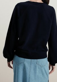 Felpa blu navy con colletto rotondo e maniche ampie, abbinata a una gonna in denim azzurro chiaro con tasche posteriori.