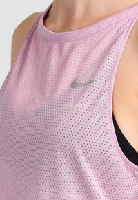 Top deportivo de color púrpura claro con una tela texturizada y transpirable. Presenta un pequeño logotipo plateado de Nike en el pecho y un diseño de espalda nadadora.