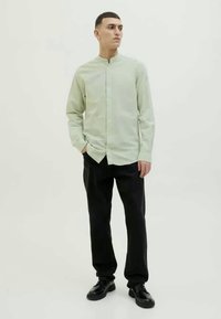 Camisa de mangas longas verde claro com colarinho mandarim, fecho de botão e um corte descontraído, combinada com calças pretas e sapatos pretos.
