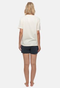 Romig kortemouwen t-shirt gecombineerd met marineblauwe gestreepte shorts. De stof lijkt zacht, met een ontspannen pasvorm en een rechte snit aan de zoom.