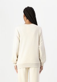 Sudadera de algodón beige con mangas largas, puños acanalados y un corte holgado. La parte posterior presenta un diseño simple y liso, sin adornos.