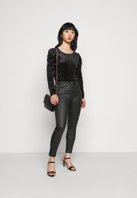 Top de veludo preto de mangas compridas com mangas bufantes e embellissements de tachas, combinado com jeans slim-fit escuros e sapatos de salto alto pretos com tiras.