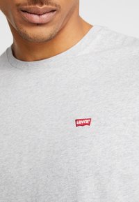 Šedé bavlněné tričko s kulatým výstřihem a malým tkaným červeným logem Levi's na hrudi, které má jemnou, hladkou texturu.