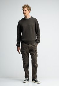 Dunkelgrauer gerippter Strickpullover, Cargohosen in gedecktem Oliv, und schwarze Sneakers mit weißen Sohlen. Lässige Passform mit Seitentaschen und strukturiertem Stoff.