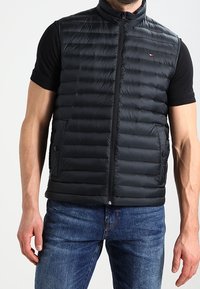 Black padded vest with a high collar, featuring a front zipper and two side pockets. Made of lightweight material with a smooth texture.