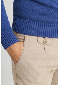 Blauwe geribde trui gecombineerd met beige broek; de trui heeft een gestructureerd breisel en de broek is voorzien van knoop- en zakdetails.