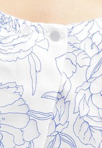 Tessuto bianco con motivo floreale blu, caratterizzato da due bottoni trasparenti all'gestruttura del collo e una superficie texturizzata.
