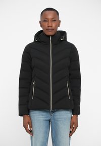 Doudoune noire avec capuche, design matelassé en chevrons, deux poches latérales zippées et détails de fermeture éclair dorés. Coupe classique.