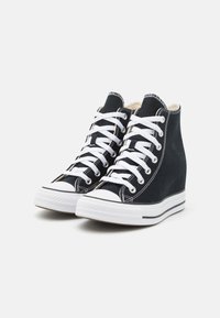 Sneakers alte in tela nera con lacci bianchi, suole in gomma bianca e cuciture a contrasto, dotate di un design con tacco a cuneo.