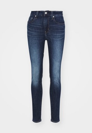 Donkerblauwe skinny jeans met een middelhoge taille, voorzien van een vervaagd patroon, vijf zakken en een metalen knoop en ritssluiting.