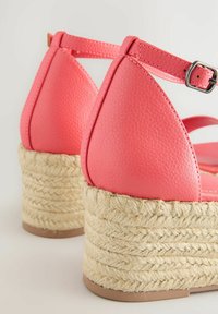 Sandales compensées en simili cuir rose avec une plateforme en jute tressé et une bride à la cheville. Surface texturée avec un design de talon triangulaire et une semelle plate.