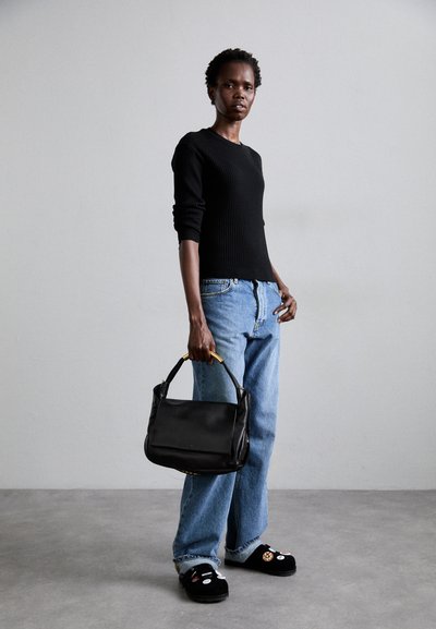 Schwarzer gerippter Pullover, hellblaue weite Jeans und schwarze Slipper mit Patches. Hält eine schwarze Handtasche mit strukturiertem Design.