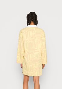 Vestido de manga longa, em amarelo pastel, com um padrão geométrico em um tom mais claro. Tecido suave com uma textura sutil, detalhe de gola na gola.