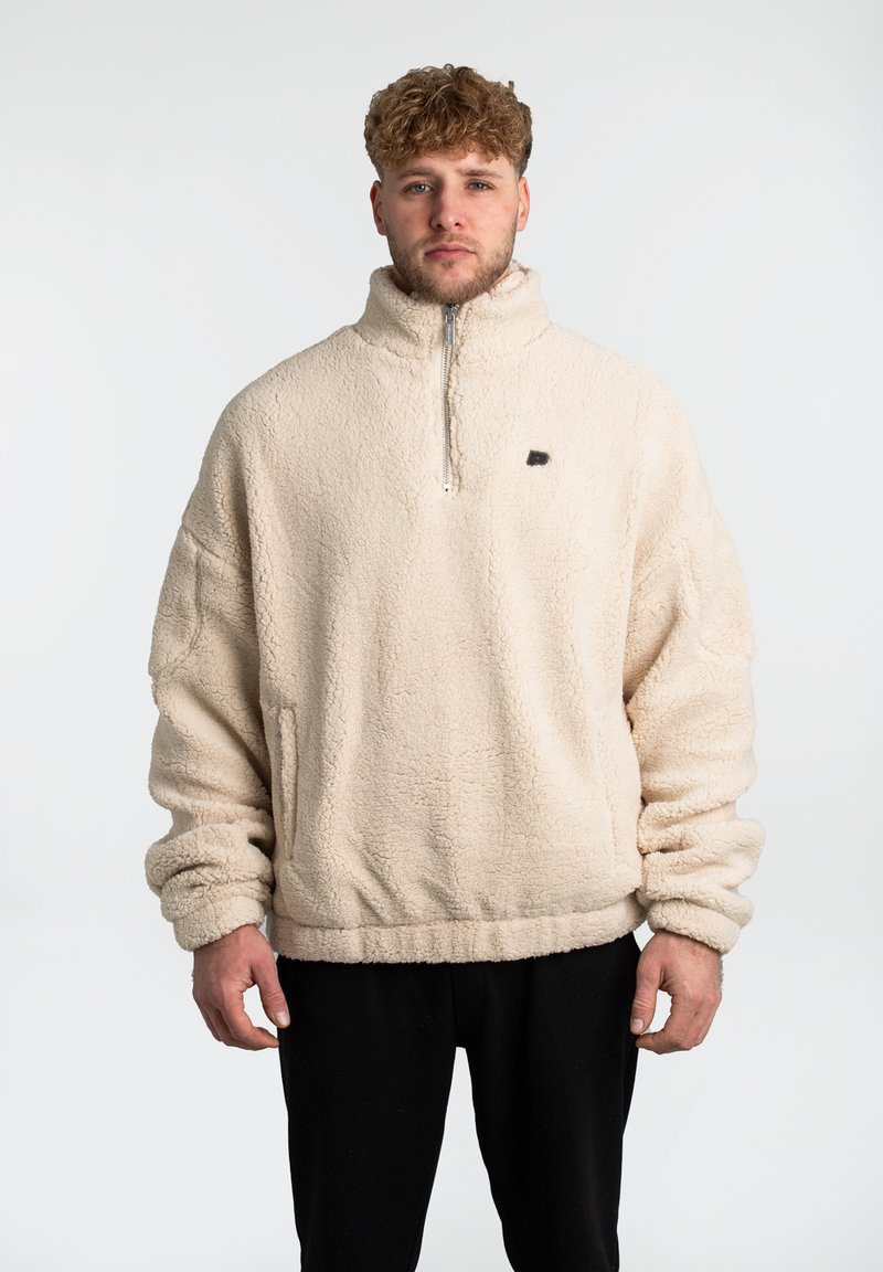 Beiger Fleece-Pullover mit hohem Kragen und halbem Reißverschluss an der Vorderseite. Hat eine lockere Passform und gerippte Bündchen. Kleines schwarzes Logo auf der Brust.