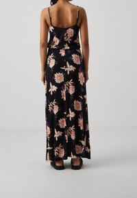 Robe maxi noire à fleurs avec bretelles spaghetti ; présente de grandes fleurs roses et blanches, une silhouette fluide et une texture de tissu lisse.