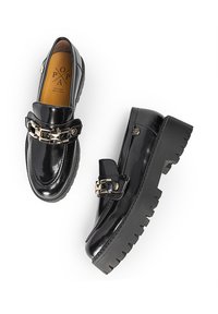 Mocasines de charol negro con suela gruesa y dentada, que presentan una correa decorativa con hebilla metálica y plantilla acolchada para mayor comodidad.