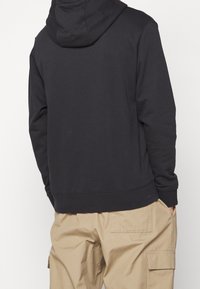 Svart, huvtröja med relaxed fit, tillverkad av mjukt tyg. Ribbad mudd och fåll, bärs tillsammans med tanfärgade cargobyxor med sidofickor.