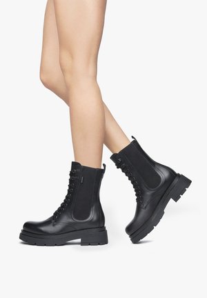 Bottines en cuir noir avec un bout rond, un laçage à l'avant et des panneaux élastiques sur les côtés. Semelle en caoutchouc épais pour la durabilité et l'adhérence.