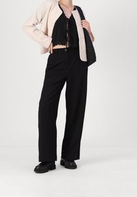 Svarta vida byxor tillsammans med en kort svart topp med scalloped kanter och en ljusrosa strukturerad cardigan. Avslutat med svarta klumpiga skor.