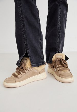 Beige kedas ar mākslīgās ādas oderi un brūnām šņorēm, saskaņotas ar tumšas denimas džinsiem, kuru apakšā ir šķirba.