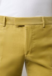 Geel ribfluweelbroek met een soepele textuur, voorzien van een tailleband en riemlussen, zijzakken en een getailleerde pasvorm.