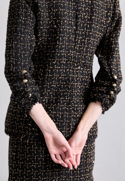 Mustan ja kullan värinen tweed-takki, jossa on teksturoitu kangas, purjeet hapsut, ja koristeelliset nappidetaalit; tiukka muotoilu, jossa on räätälöity design.