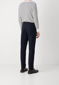 Marina chinos med rak passform, bomullstyg, bälteshål och bakfickor, i kombination med en vit och marinrandig långärmad skjorta.