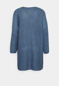 Długi sweter dzianinowy w jasnoniebieskim kolorze, z teksturowanym wzorem i luźnym krojem. Tył ma prosty, okrągły dekolt.