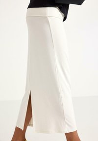 Valkoinen puuvillasekoiteskirt, jossa on korkea vyötärö, sivurako ja minimalistinen muotoilu. Sileä tekstuuri, polvenpituinen ja istuva leikkaus.