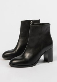 Bottines en cuir noir avec un bout pointu, un talon block moyen et une fermeture éclair décorative sur le côté, présentant une texture lisse et un design minimaliste.