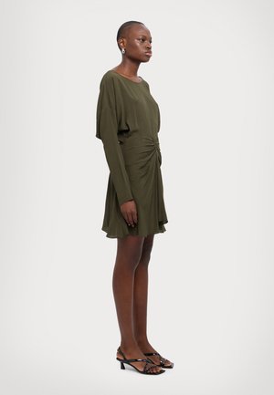 Rochie verde măsliniu, cu mânecă lungă, cu un design adunat la talie, având o croială relaxată și o fustă fluidă. Asortată cu sandale negre cu toc.