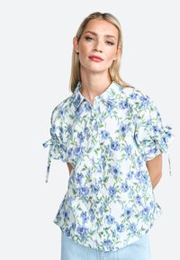 Floral blouse featuring blue and green patterns on a light background, short sleeves with ties, and a button-up collar design.