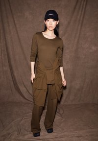 Olijfgroene, lange mouwen top gecombineerd met bijpassende broek met een gestrikt detail op de taille; zwarte pet met tekst; gladde stofstructuur.