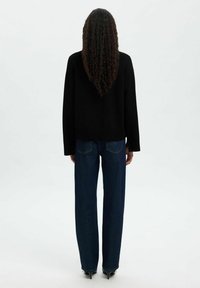 Svart tröja med axlar som hänger ner, matchad med högmidjade, raka mörkblå jeans och spetsiga svarta klackar.