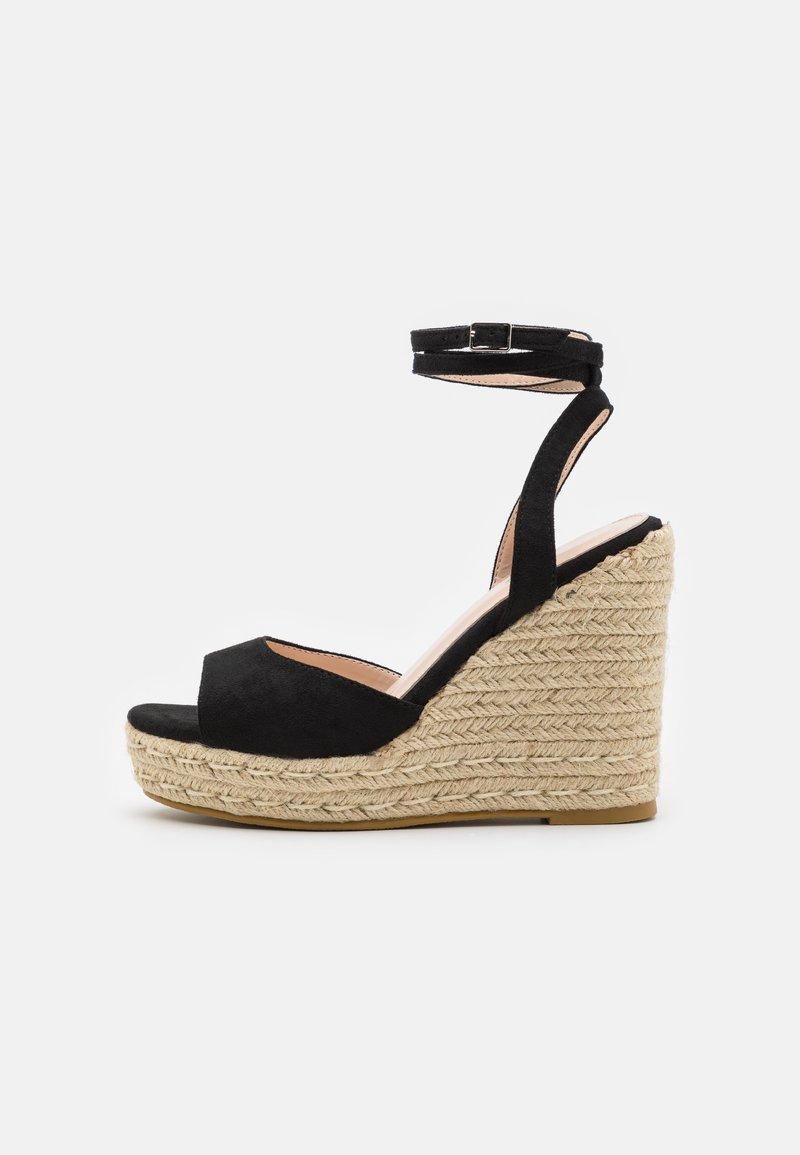 Sandales compensées en daim noir avec bout ouvert, bride à la cheville et plateforme en jute tressé. Des détails texturés sur la semelle compensée ajoutent de la dimension.