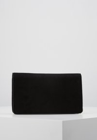 Bolso de mano rectangular negro con textura suave, reposando sobre un pedestal cúbico blanco contra un fondo gris sencillo.