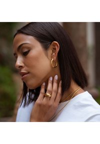 Goldene Creolen, gestapelte Halsketten und ein klobiger goldener Ring. Glatte Textur mit glänzendem Finish. Elegantes, minimalistisches Design.