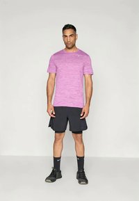 Camiseta deportiva rosa con un patrón texturizado, combinada con pantalones cortos negros, calcetas negras y zapatillas deportivas negras. Diseño sencillo, de mangas cortas.