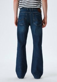 Jeans de denim azul oscuro con un diseño de pierna ancha, que cuentan con dos bolsillos traseros y detalles sutiles de desgaste. Trabilla para cinturón y etiqueta de cuero en la cintura.