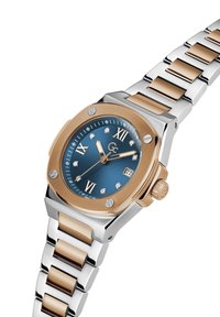 Zegarek analogowy z niebieską tarczą, złotymi akcentami, rzymskimi cyframi, diamentowymi znacznikami oraz bransoletą metalową w dwóch kolorach z polerowanymi ogniwami.