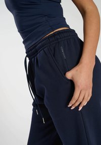 Marineblaue Jogginghosen mit lockerer Passform, elastischem Bund und Kordelzug. Weicher Stoff mit Seitentaschen und einem sichtbaren Logo-Tag an der Hüfte.