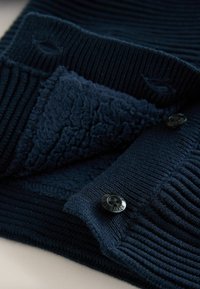 Marine gebreide cardigan met ribbelstructuur, voorzien van zachte fleece voering en zwarte knopen met geëmbosseerde tekst.